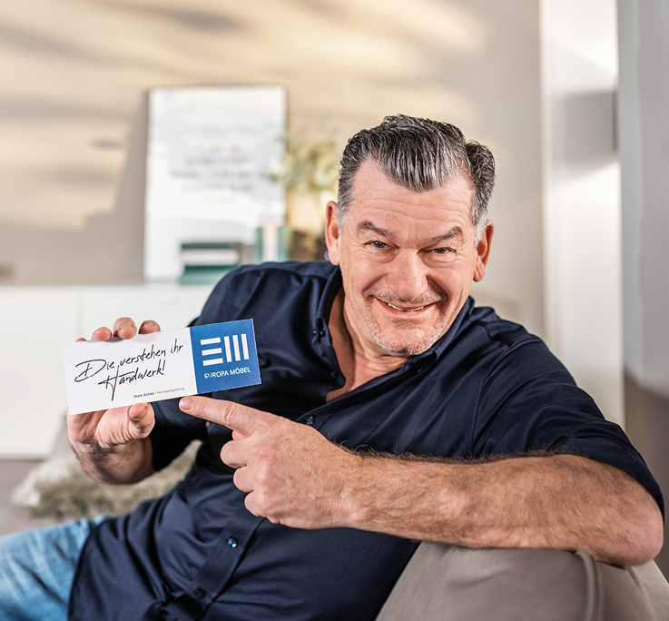 Mark Kuehler - EMC-Markenbotschafter EMC-Markenbotschafter Mark Kuehler mit Schild in der Hand auf Sofa.