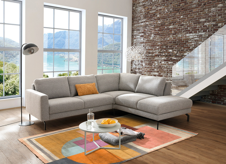 Graues Activineo Ecksofa mit passendem Couchtisch vor grosser Fensterfront in Wohnzimmer.