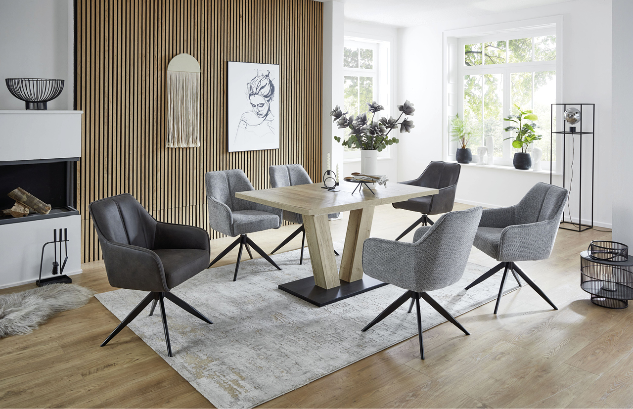 Stilvoller Essbereich mit rechteckigem Holz-Esstisch, sechs gepolsterten Drehstühlen in Grau und Anthrazit, hellen Holzböden, Wandverkleidung in Holzlamellen und großen Fenstern mit Tageslicht.