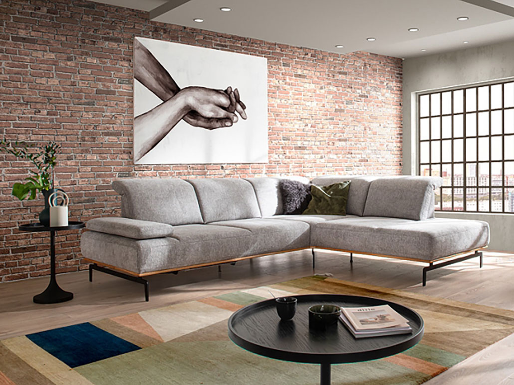 Design-Ecksofa in Grau vor Backsteinwand – modernes Wohnzimmer im Loftstil Modernes Wohnzimmer mit grauem Design-Ecksofa, Backsteinwand, großem Wandbild und geometrischem Teppich – stilvolle Loft-Einrichtung, gemütliche Sofalandschaft mit urbanem Flair und klaren Linien.